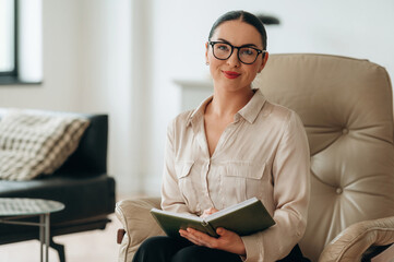In glasses, front view. Woman in formal clothes is in the modern big room