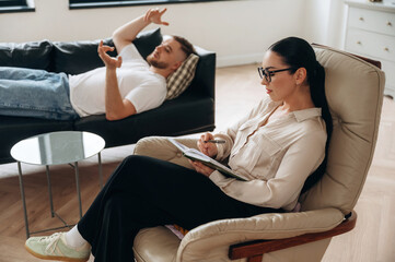Listening, making notes. Man is lying down at couch and talking, at psychologist appointment