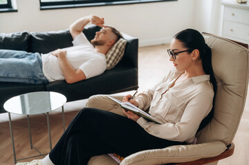 Listening, making notes. Man is lying down at couch and talking, at psychologist appointment