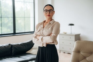 Arms crossed, standing. Woman in formal clothes is in the modern big room