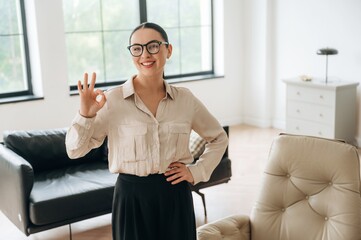 Okay hand sign. Woman in formal clothes is in the modern big room