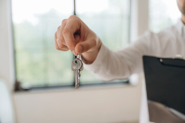 Front view, holding keys for new home. Real estate agent is in the new room
