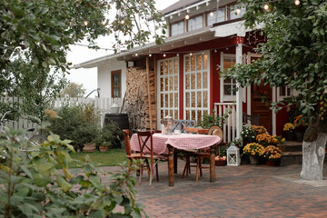 Empty outdoor table with checkered tablecloth standing in front of rustic village house surrounded...