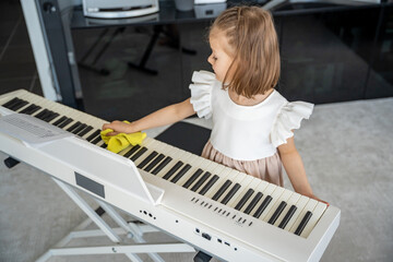 Little girl carefully cleaning her piano at home in the living room. Early childhood education through music includes care, responsibility and respect for the instrument.