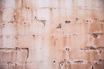 Paint peeling from faded pink brick wall