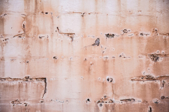 Paint peeling from faded pink brick wall