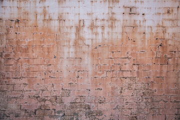 Paint peeling from faded pink brick wall
