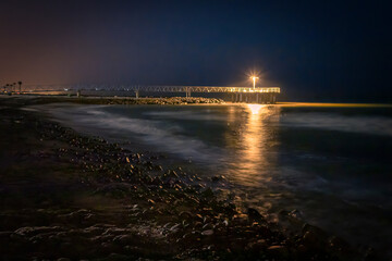 pantalan en la playa de xilxes por la noche con el mar iluminado por la luz de la farola y la playa...