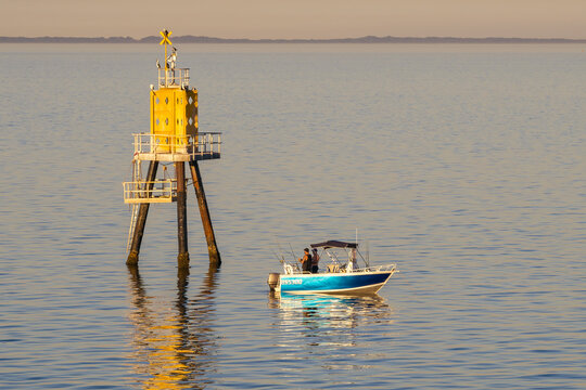 Men fishing from a small boat on calm water near a channel marker