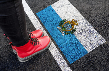 a woman with a boots standing on asphalt next to flag of San Marino and border
