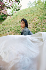 Young man in stylish grey outfit enjoys a serene moment in a park full of blossoms