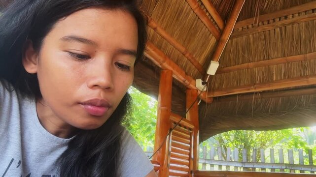 Filipina woman eats soup in arbor at tropical cottage