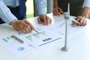 Businesspeople reviewing ESG investment charts and wind turbine model; sustainable growth strategy meeting.