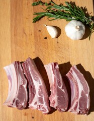 Several pieces of raw lamb ribs placed on a wooden cutting board, accompanied by a clove of garlic...