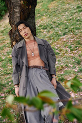 Stylish young man relaxes under a tree in a park during a sunny afternoon