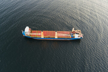 Aerial shot from a drone: a blue cargo ship with red decks sails through the dark and calm waters...