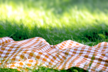 Orange checkered picnic towel plaid on grass, tablecloth outdoors.Food advertisement summer template.