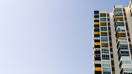 Tall residential apartments with geometric, colorful balconies under clear blue sky, copy space for...
