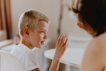 Young mother helps her hard-of-hearing son with schoolwork at home. A natural, heartfelt moment of...