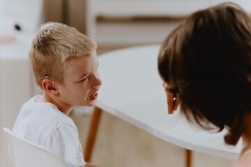 Young mother helps her hard-of-hearing son with schoolwork at home. A natural, heartfelt moment of...