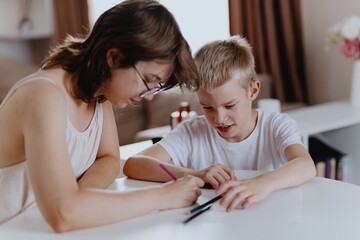 Young mother helps her hard-of-hearing son with schoolwork at home. A natural, heartfelt moment of...