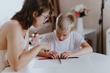 Young mother helps her hard-of-hearing son with schoolwork at home. A natural, heartfelt moment of...