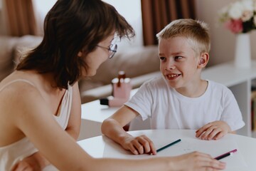 Young mother helps her hard-of-hearing son with schoolwork at home. A natural, heartfelt moment of...