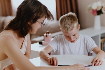 Young mother helps her hard-of-hearing son with schoolwork at home. A natural, heartfelt moment of...