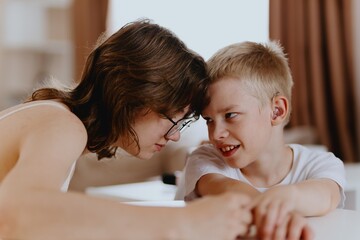 Young mother helps her hard-of-hearing son with schoolwork at home. A natural, heartfelt moment of...