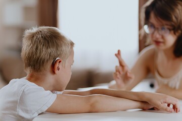 Young mother helps her hard-of-hearing son with schoolwork at home. A natural, heartfelt moment of...
