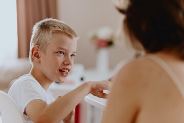 Young mother helps her hard-of-hearing son with schoolwork at home. A natural, heartfelt moment of...