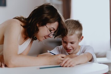 Young mother helps her hard-of-hearing son with schoolwork at home. A natural, heartfelt moment of...