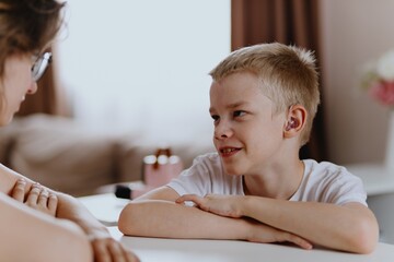 Young mother helps her hard-of-hearing son with schoolwork at home. A natural, heartfelt moment of...