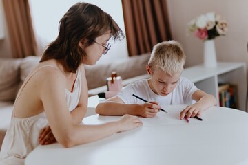 Young mother helps her hard-of-hearing son with schoolwork at home. A natural, heartfelt moment of...
