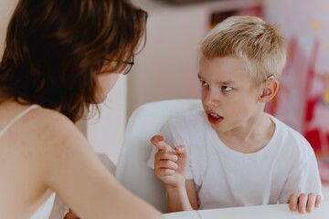 Young mother helps her hard-of-hearing son with schoolwork at home. A natural, heartfelt moment of...