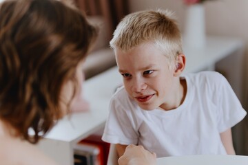 Young mother helps her hard-of-hearing son with schoolwork at home. A natural, heartfelt moment of...