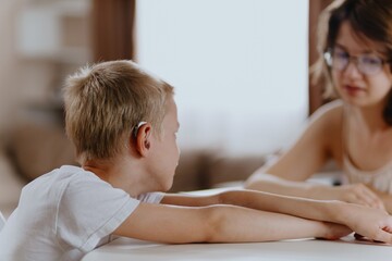 Young mother helps her hard-of-hearing son with schoolwork at home. A natural, heartfelt moment of...