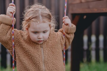 Beautiful 3-year-old girl playing on a neighborhood playground swinging, running on the grass, and enjoying fresh air. A joyful, natural moment full of real emotions and unaltered beauty