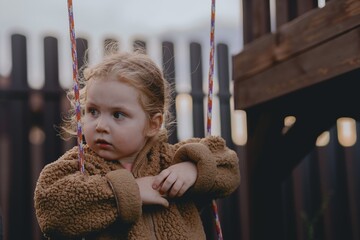 Beautiful 3-year-old girl playing on a neighborhood playground swinging, running on the grass, and enjoying fresh air. A joyful, natural moment full of real emotions and unaltered beauty