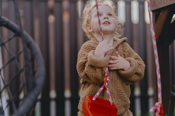 Beautiful 3-year-old girl playing on a neighborhood playground swinging, running on the grass, and enjoying fresh air. A joyful, natural moment full of real emotions and unaltered beauty