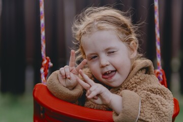 Beautiful 3-year-old girl playing on a neighborhood playground swinging, running on the grass, and enjoying fresh air. A joyful, natural moment full of real emotions and unaltered beauty