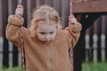 Beautiful 3-year-old girl playing on a neighborhood playground swinging, running on the grass, and enjoying fresh air. A joyful, natural moment full of real emotions and unaltered beauty