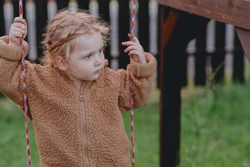 Beautiful 3-year-old girl playing on a neighborhood playground swinging, running on the grass, and enjoying fresh air. A joyful, natural moment full of real emotions and unaltered beauty
