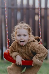 Beautiful 3-year-old girl playing on a neighborhood playground swinging, running on the grass, and enjoying fresh air. A joyful, natural moment full of real emotions and unaltered beauty