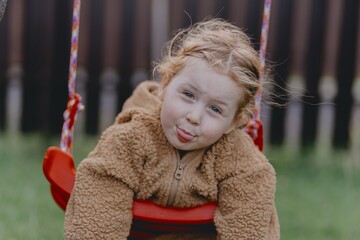 Beautiful 3-year-old girl playing on a neighborhood playground swinging, running on the grass, and enjoying fresh air. A joyful, natural moment full of real emotions and unaltered beauty