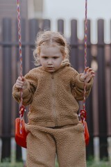 Beautiful 3-year-old girl playing on a neighborhood playground swinging, running on the grass, and enjoying fresh air. A joyful, natural moment full of real emotions and unaltered beauty