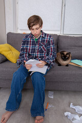 Boy sits on couch with cat while working on homework in a cozy living room during afternoon