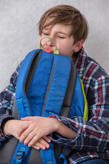 A schoolboy hugs his cold backpack with annoyance and grimaces.