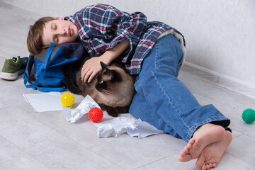 Young boy lies on the floor resting with a cat surrounded by colorful toys and crumpled paper in a cozy indoor setting
