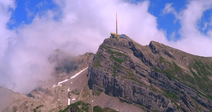 Stunning mountain peak covered in clouds with a lookout tower at the summit during a bright sunny day in the Swiss Alps